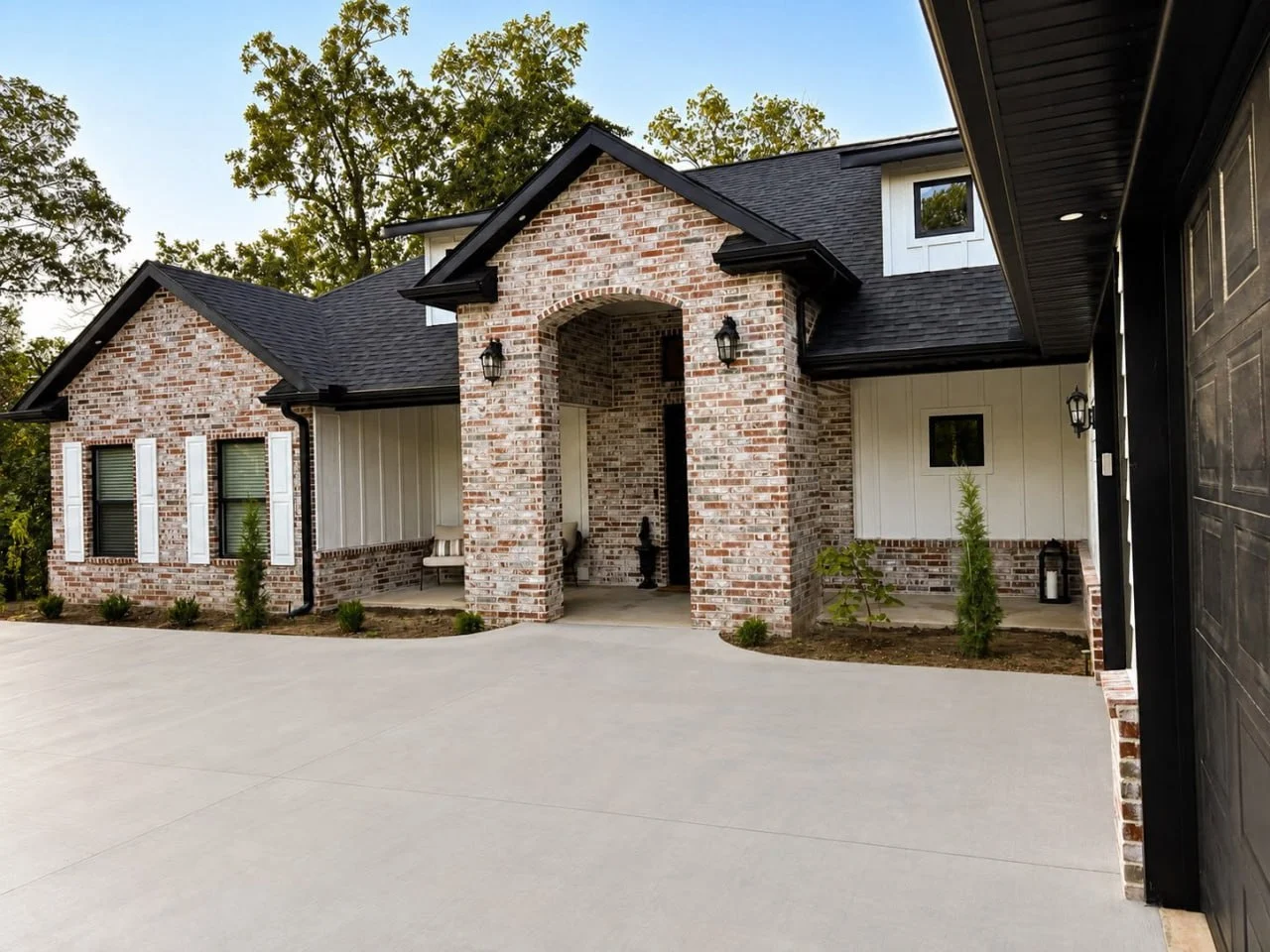 Modern brick home exterior with arched entry, black roof, and attached garage