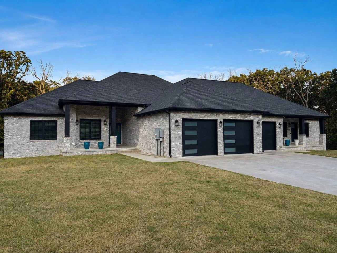 Modern single-story brick home with dark roof, black garage doors, and a wide driveway